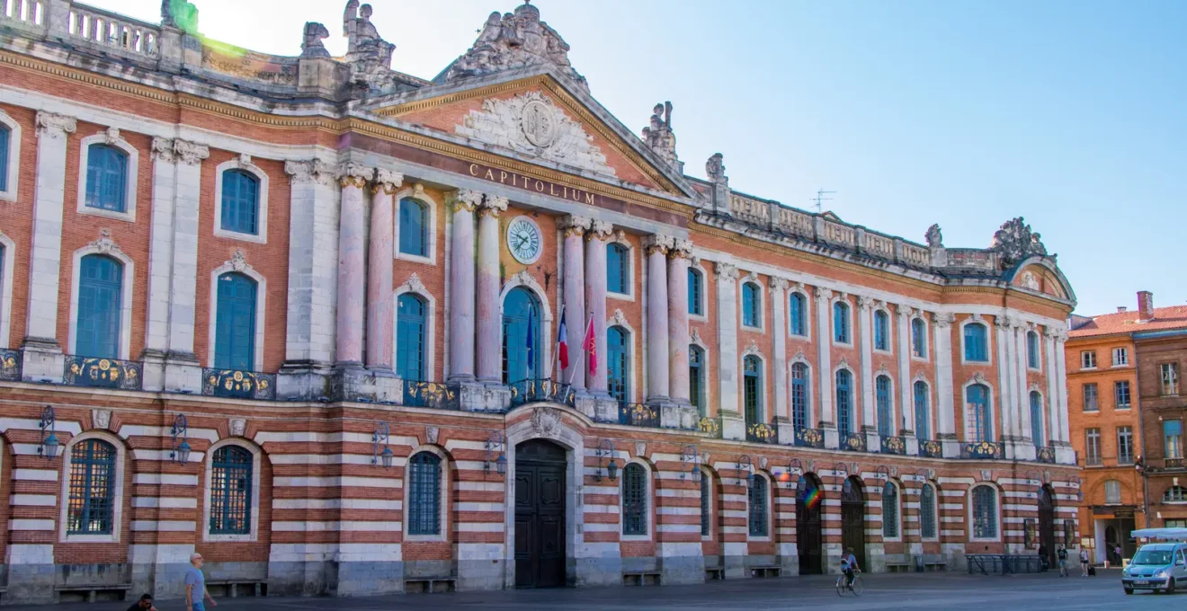 Un couple avec valises marche dans une rue de briques roses de Toulouse.